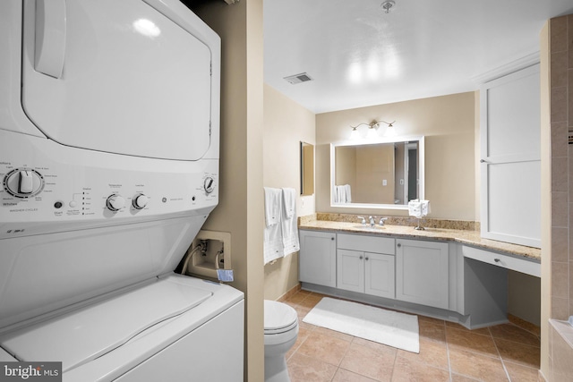 bathroom featuring tile patterned flooring, stacked washer and dryer, vanity, and toilet