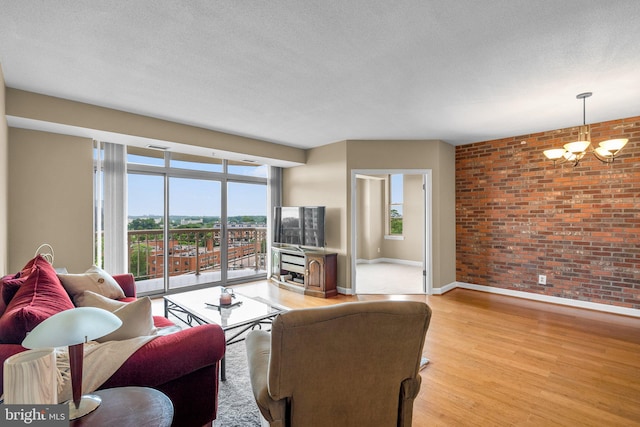 living room with a textured ceiling, light hardwood / wood-style floors, an inviting chandelier, and brick wall