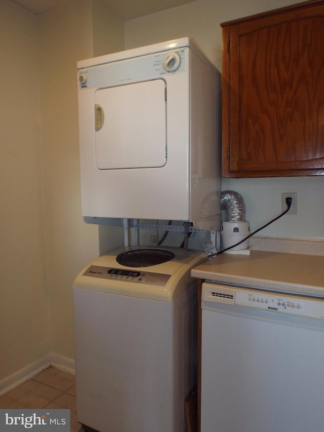 laundry room featuring stacked washing maching and dryer, light tile patterned flooring, baseboards, and cabinet space