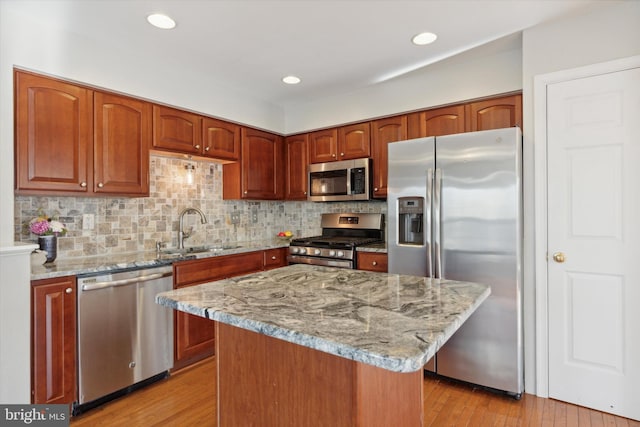 kitchen with sink, a center island, stainless steel appliances, light stone counters, and light wood-type flooring