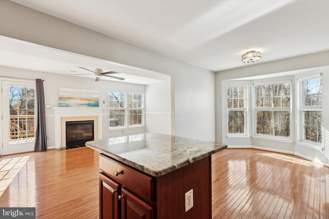 kitchen with light stone counters, a center island, ceiling fan, and light hardwood / wood-style floors