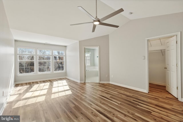 unfurnished bedroom featuring a spacious closet, ceiling fan, light wood-type flooring, and vaulted ceiling