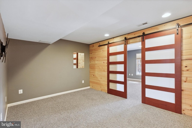 carpeted spare room with wood walls and a barn door