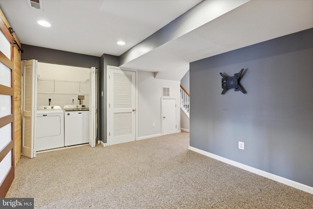 basement featuring light carpet, a barn door, and washing machine and clothes dryer