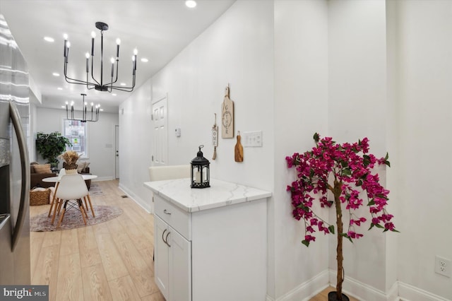 kitchen with pendant lighting, light hardwood / wood-style floors, light stone counters, white cabinetry, and a chandelier