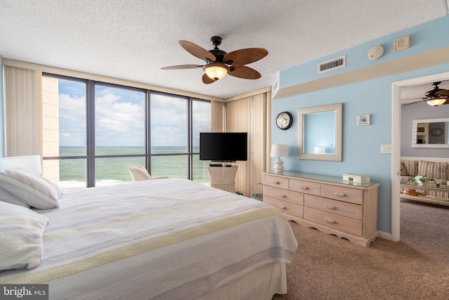 carpeted bedroom with a textured ceiling, a wall of windows, and ceiling fan