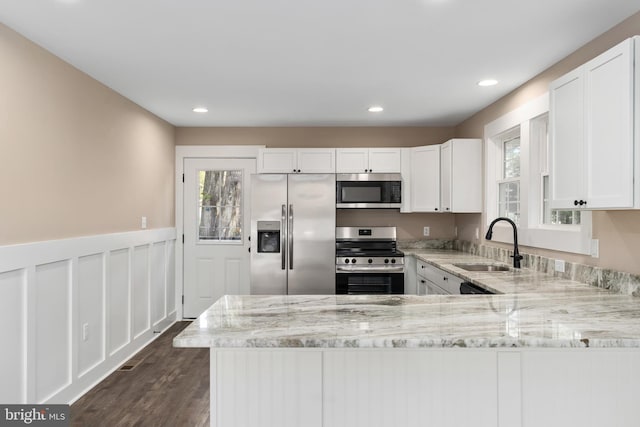 kitchen with light stone counters, stainless steel appliances, sink, and white cabinetry