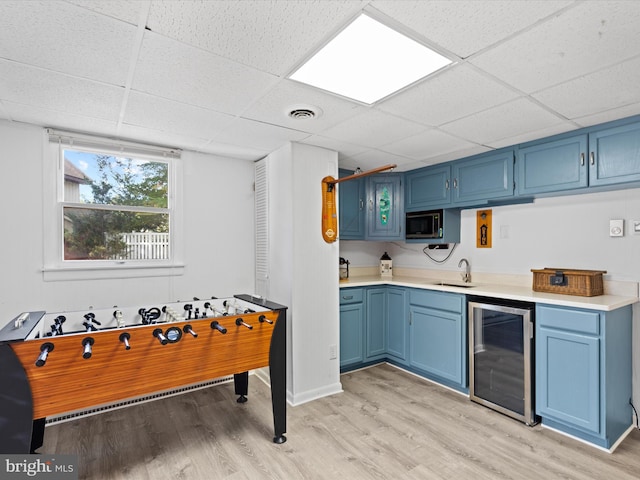 kitchen featuring a drop ceiling, beverage cooler, light hardwood / wood-style flooring, and blue cabinetry