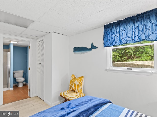 bedroom featuring a closet, connected bathroom, light hardwood / wood-style floors, and a paneled ceiling