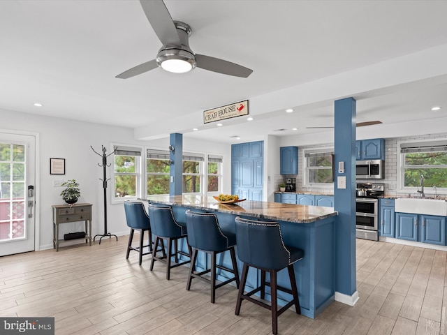 kitchen featuring blue cabinets, stainless steel appliances, a kitchen bar, and decorative backsplash