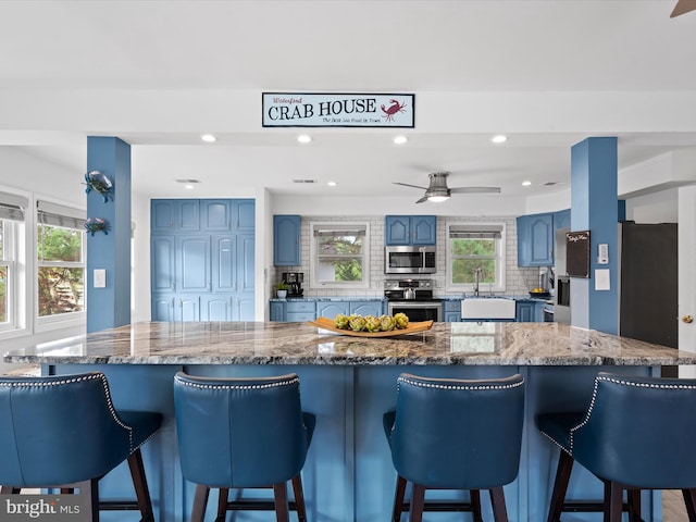 kitchen with ceiling fan, tasteful backsplash, a kitchen breakfast bar, sink, and stainless steel appliances