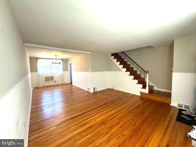 unfurnished living room featuring an inviting chandelier, wood-type flooring, and a wall mounted AC