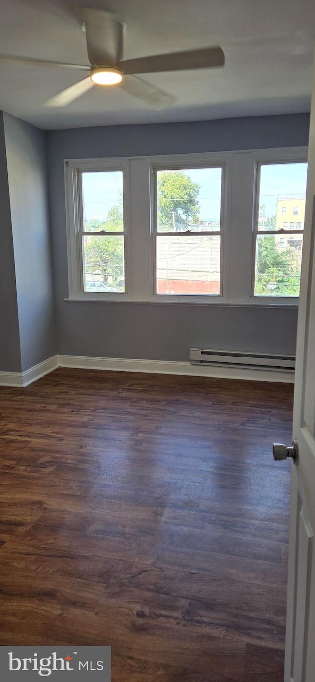 empty room with ceiling fan, baseboard heating, and dark wood-type flooring