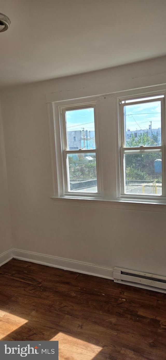 unfurnished room with a baseboard heating unit and wood-type flooring