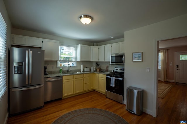 kitchen featuring wood-type flooring, light stone counters, sink, white cabinetry, and appliances with stainless steel finishes