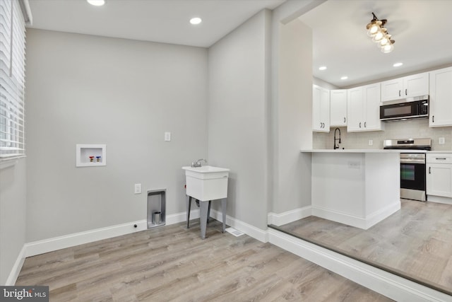 kitchen with white cabinets, kitchen peninsula, backsplash, appliances with stainless steel finishes, and light wood-type flooring