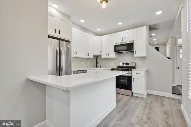 kitchen featuring appliances with stainless steel finishes, decorative backsplash, light wood-type flooring, and white cabinets