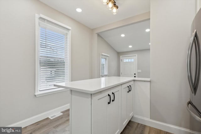 kitchen featuring light hardwood / wood-style floors, white cabinets, stainless steel refrigerator, kitchen peninsula, and lofted ceiling