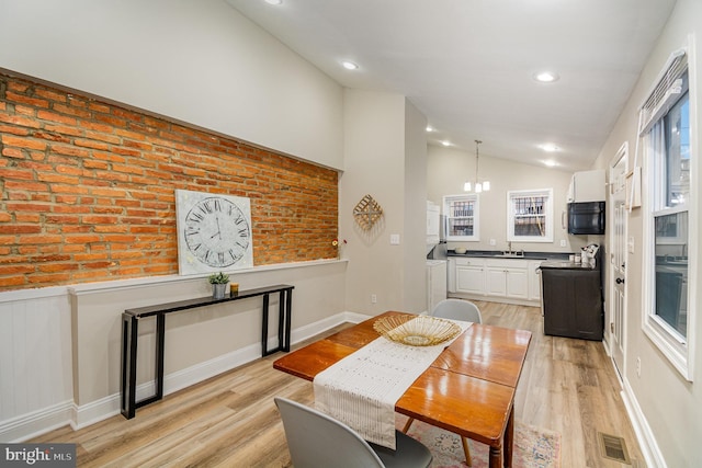 dining room with vaulted ceiling, sink, a notable chandelier, and light hardwood / wood-style floors