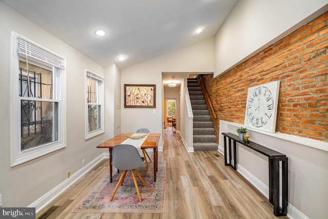 interior space featuring lofted ceiling, brick wall, and light wood-type flooring