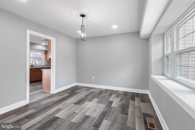 unfurnished dining area featuring a notable chandelier, sink, and dark hardwood / wood-style flooring