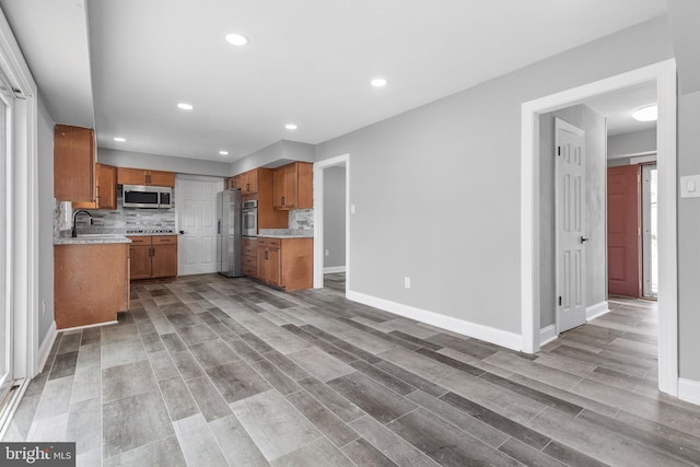 kitchen with appliances with stainless steel finishes, backsplash, light wood-type flooring, and sink