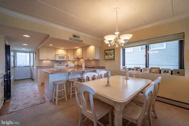 dining space with sink, a baseboard heating unit, light colored carpet, a notable chandelier, and crown molding