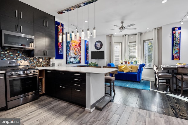 kitchen featuring a breakfast bar, light wood-type flooring, kitchen peninsula, hanging light fixtures, and stainless steel appliances