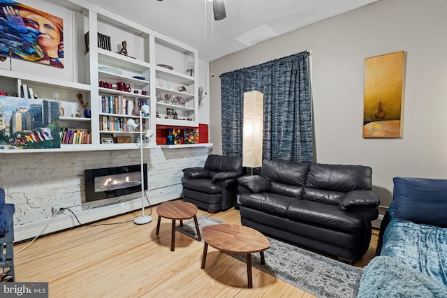 living room featuring wood-type flooring, a stone fireplace, and ceiling fan