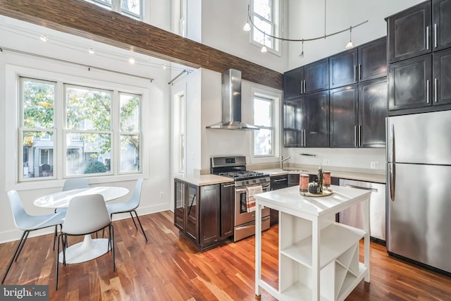 kitchen featuring appliances with stainless steel finishes, a wealth of natural light, wall chimney range hood, and a towering ceiling