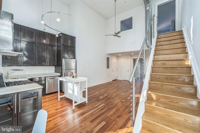 kitchen featuring stainless steel appliances, ventilation hood, decorative light fixtures, light wood-type flooring, and high vaulted ceiling