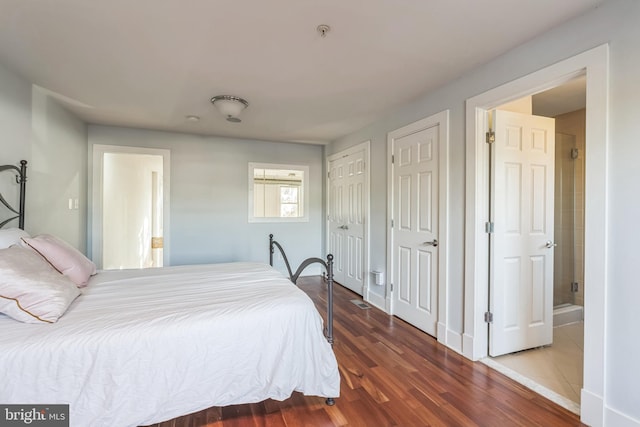 bedroom featuring ensuite bath, dark wood-type flooring, and multiple closets