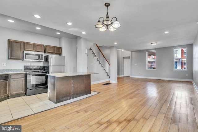 kitchen featuring stainless steel appliances, a kitchen island, decorative light fixtures, and light hardwood / wood-style flooring