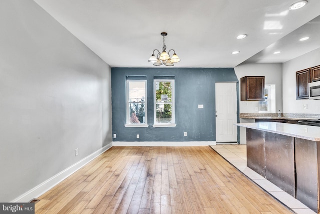 kitchen with dark brown cabinets, pendant lighting, a notable chandelier, and light wood-type flooring