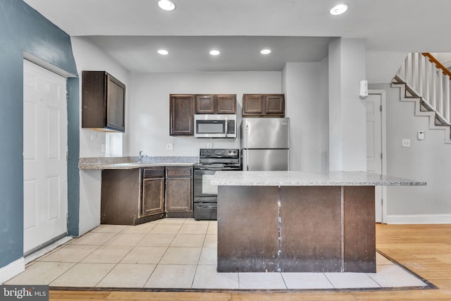 kitchen with light tile patterned floors, appliances with stainless steel finishes, dark brown cabinets, a center island, and light stone counters