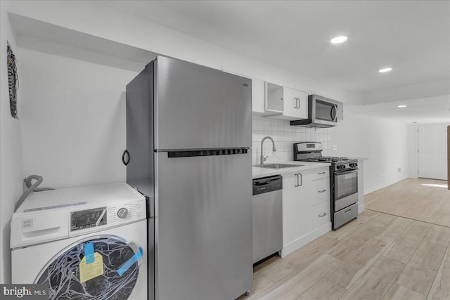 kitchen featuring washer / dryer, white cabinets, sink, light hardwood / wood-style floors, and appliances with stainless steel finishes