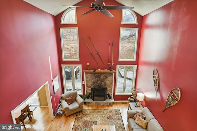 living room featuring light hardwood / wood-style floors, a stone fireplace, high vaulted ceiling, and ceiling fan