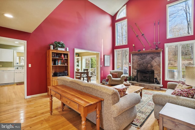 living room with high vaulted ceiling, light hardwood / wood-style flooring, and a stone fireplace