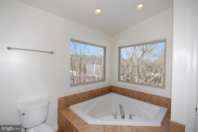 bathroom with tiled bath, vaulted ceiling, and toilet