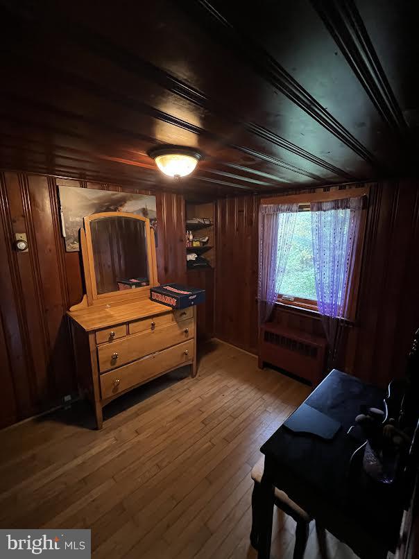 bedroom with hardwood / wood-style floors, radiator, and wood walls