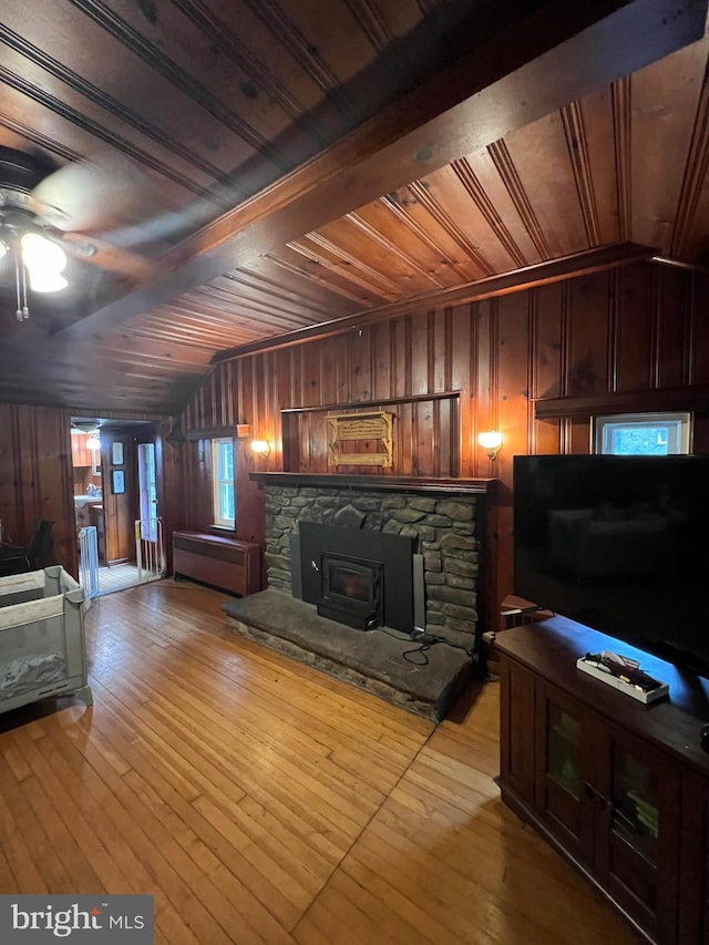 living room with wood walls, a wood stove, vaulted ceiling, light wood-type flooring, and wood ceiling