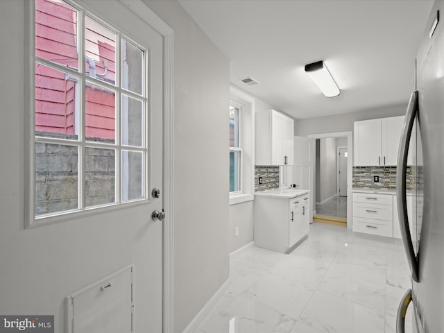 interior space featuring stainless steel fridge, tasteful backsplash, and white cabinets