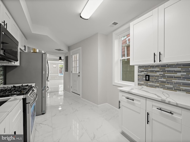 kitchen with plenty of natural light, gas range, light stone countertops, and white cabinetry