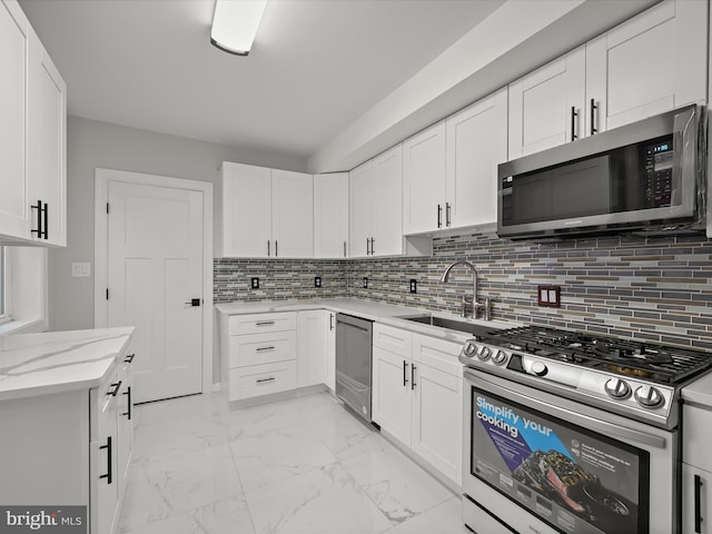 kitchen with sink, tasteful backsplash, white cabinetry, appliances with stainless steel finishes, and light stone countertops