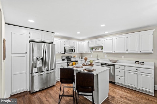 kitchen featuring appliances with stainless steel finishes, a breakfast bar, white cabinets, dark hardwood / wood-style flooring, and a center island