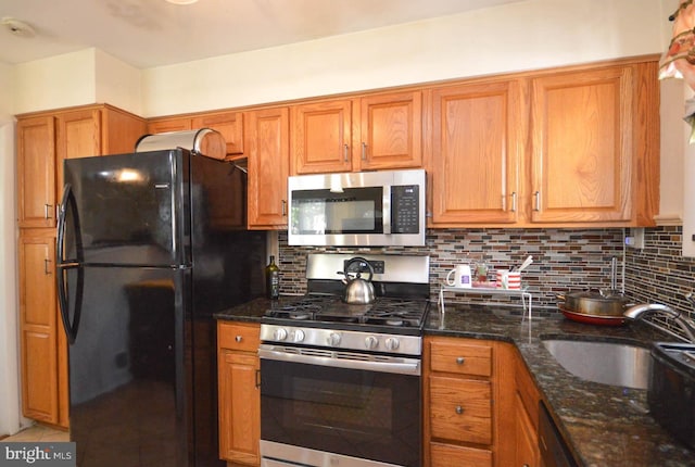 kitchen featuring dark stone countertops, backsplash, appliances with stainless steel finishes, and sink