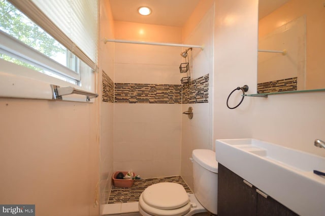 bathroom featuring a tile shower, vanity, and toilet