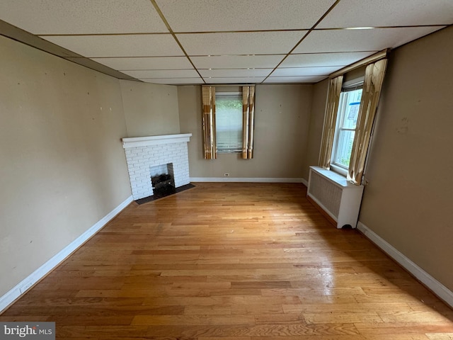 unfurnished living room featuring a paneled ceiling, radiator, light hardwood / wood-style flooring, and a brick fireplace