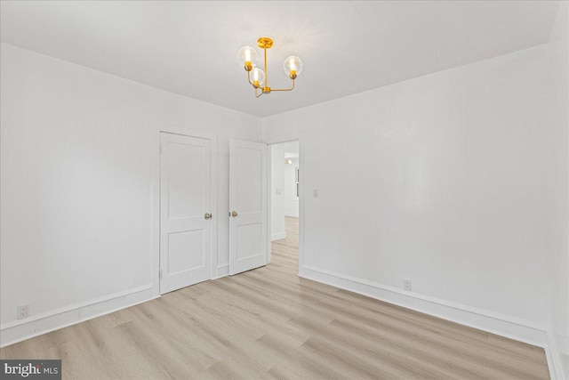 empty room with light hardwood / wood-style flooring and a chandelier