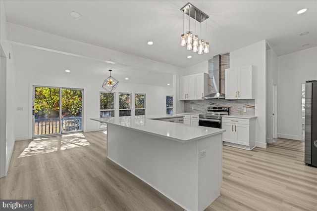 kitchen with wall chimney exhaust hood, hanging light fixtures, white cabinets, appliances with stainless steel finishes, and light hardwood / wood-style floors